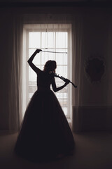 Pretty slender young woman with violin at window. Female in stage image in sunlight. Emotional girl...