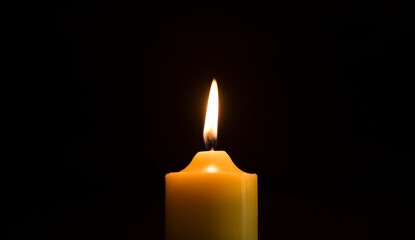 One candle is lit in the dark or on a black background.