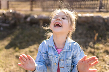 A seven year old girl laughs and rejoices in the spring on the street in a denim jacket.