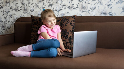 A first grader girl studies at home on distance learning using a laptop. Children education concept.