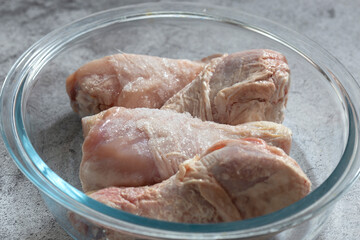 Frozen raw chicken defrosting in a glass dish.  On a concrete background