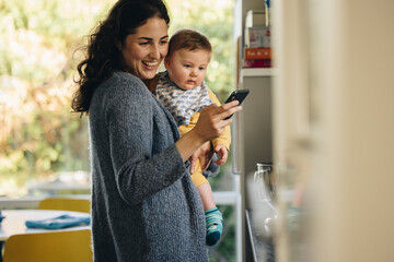 Mother carrying baby texting on her cell phone