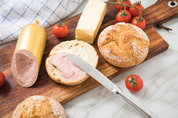 Feine Kalbsleberwurst auf Weizen Rosen Brötchen dazu Tomaten, Butter und Messer mit Holzbrett,...