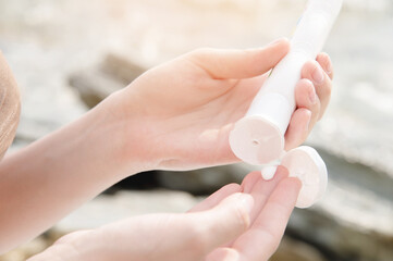 Close-up young caucasian woman squeezes sunscreen out of a tube on the sea beach on a sunny day. UV protection