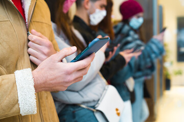 Mid section of millennials using smartphone outdoors. Young people in new normal addicted by smartphone and social media application wearing protective face mask against coronavirus concept.