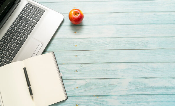 top view of a workspace with laptop computer idea notebook and pen, with a red apple on a blue vintage wooden table. Business concept. Back to school - Powered by Adobe