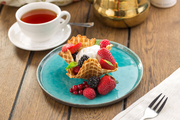 ice cream in waffle cone with fresh berries and cup of tea on wooden table