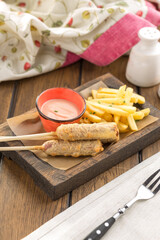 corn dog sausage on a stick with french fries on wooden table