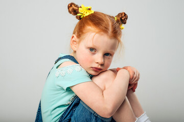 Little girl with red hair on a gray background. Sadness hugging his legs with gooks.