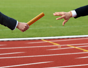Businessmen pass on the baton in relay race in stadium - obrazy, fototapety, plakaty