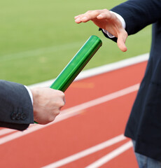 Businessmen pass on the baton in relay race in stadium