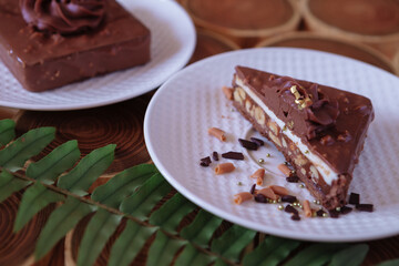 chocolate dessert in a cut with filling of caramel, nuts and nougats. The cake is covered with chocolate on a wooded background with a morning natural light