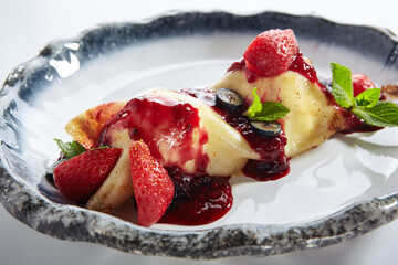 French Style Crepes - Cream Crepes with Berry and Fruit. Pancake Breakfast on white and blue plate isolated on white background. Mixed berry crepes garnished with mint and sweet sauce.