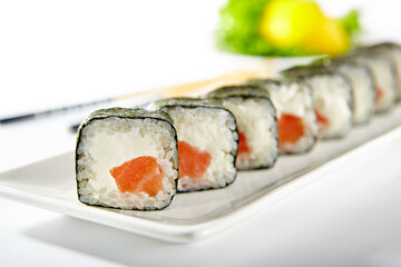 Philadelphia Sushi Roll made with Smoked Salmon. Maki sushi with nori seaweed outside, salmon and cream cheese inside. White plate with wooden chopsticks on white table.