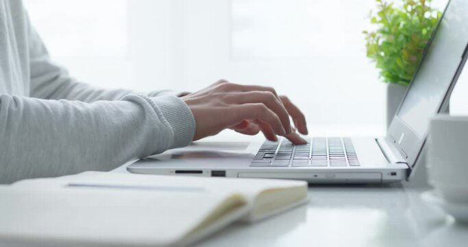 Cropped female hands write in a notebook and work on a laptop. A woman manager makes a note and uses a computer keyboard while sitting at her desk at home.