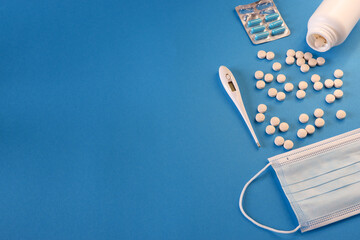 Medicine and health concept. Blister with capsules, pills, thermometer and medical mask on a blue background. Place for your text.