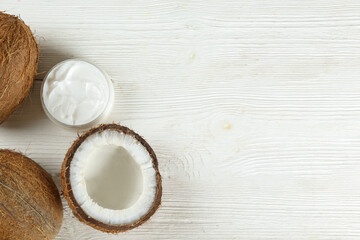 Fototapeta na wymiar Coconut as a food source and cosmetic product. Cracked fruit with a jar of moisturizing cream on wood textured table. Close up, top view, copy space, flat lay, background.