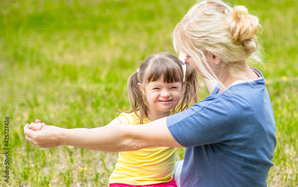 Wall mural happy family. little girl with syndrome down and her mother play together in a summer park