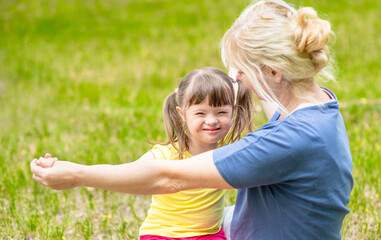 Happy family. Little girl with syndrome down and her mother play together in a summer park