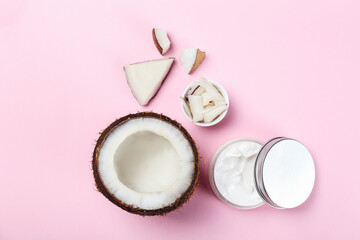 Coconut as a food source and cosmetic product. Cracked fruit with a jar of moisturizing cream on pink tabletop. Close up, top view, copy space, flat lay, background.