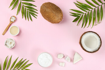 Coconut as a food source and cosmetic product. Whole and cracked fruit, a jar of moisturizing cream and oil, spoon and palm leaf on pink tabletop. Close up, top view, copy space, flat lay, background.