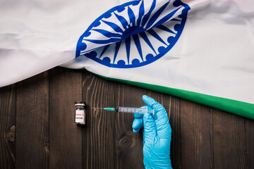 Hands of doctor wearing gloves holding coronavirus (COVID-19) vial vaccine and syringe with flag India on wooden background, India Vaccination