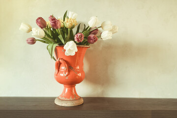 A bouquet of tulip flowers in a red vintage ceramic vase on the background of a light wall in the room