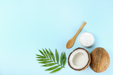 Coconut as a food source and cosmetic product. Cracked fruit, a jar of moisturizing cream, wooden spoon and a palm leaf on blue tabletop. Close up, top view, copy space, flat lay, background.