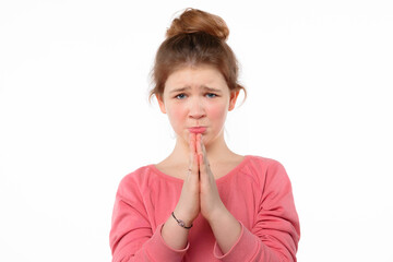 Fototapeta premium Cute young girl pleads for something, keeps palms pressed together in front of her, has regretful expression