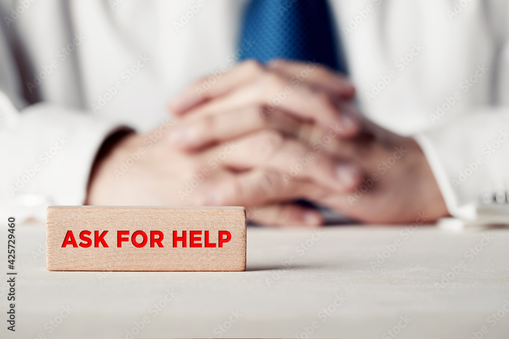 Poster the message ask for help written on a wooden block in front of a businessman with crossed hands.