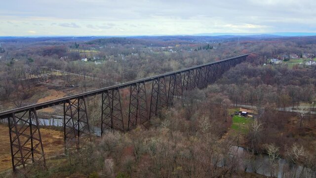 Aerial drone video footage of a train bridge viaduct running over a valley in the Appalachain Mountains during early spring on a cloud day, surrounded by mountains and farmland. 