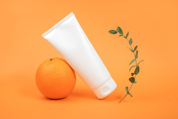 White blank cosmetic bottle, tube of cream, lotion for body, face or hand, orange fruit and green branch eucalypt. Concept cosmetics with vitamin C, antioxidants or anti-cellulite. Mockup Copy space