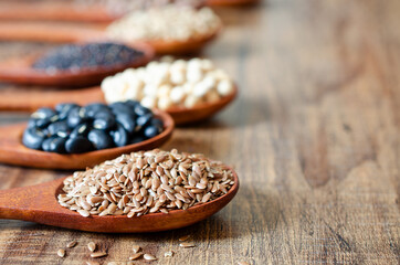 Closed up dry organic flax seed in wooden spoon with blur black bean, soybean, quinoa, and chickpea, for healthy food or agricultural product concept