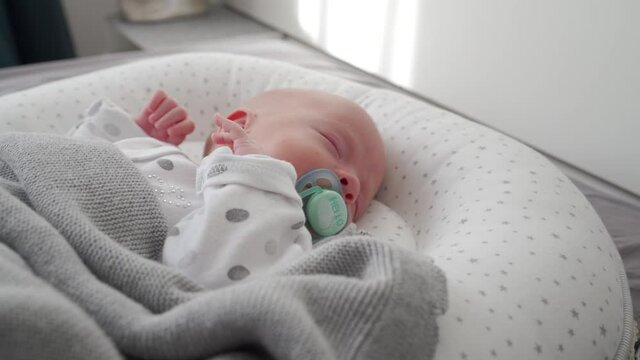 Adorable baby boy lying in baby pod nest newborn cocoon, infant sleep safety, co-sleeping bed sharing with baby. High quality 4k footage