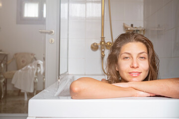 Close up portrait of a beautiful smiling young woman relaxing in a bathtub. Happy brunette female...