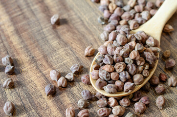 Dry organic brown chickpea seeds in wooden spoon on grunge background