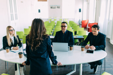 Confident businesswoman commenting marketing results to colleagues at meeting. Rear view.