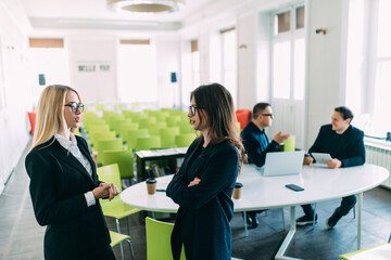 Two Businesswomen having informal meeting in modern office in front of team