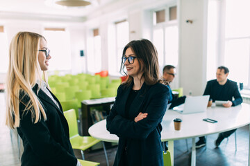 Two Businesswomen having informal meeting in modern office in front of team