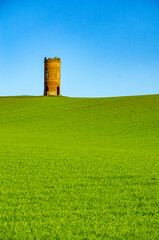 Fototapeta na wymiar Wilder's Folly, a brick built structure, stands and the distance in a green field against a vibrant blue sky