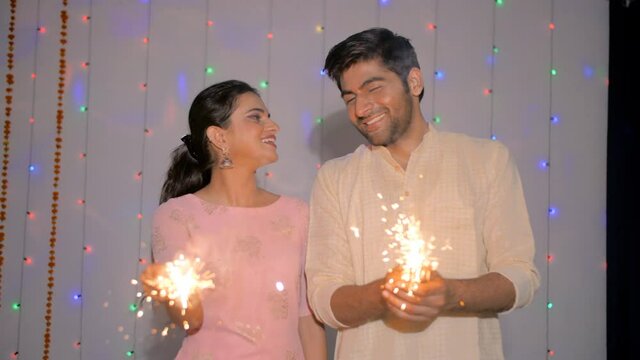 Modern husband-wife celebrating the festival of Deepawali at their home. Medium shot of an Indian couple happily burning firecrackers/sparklers during the Hindu festival Diwali