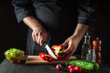 Close-up of a chef hands cutting peppers on cutting board. Professional preparation of salad in the kitchen in a restaurant or cafe