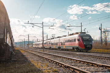 Fototapeta na wymiar Red modern passenger train rushing through industrial district on a sunny afternoon