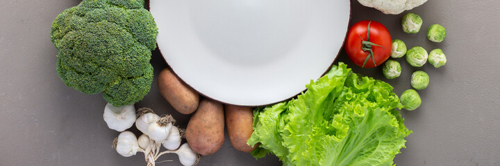 Fresh farm organic vegetables, healthy food banner, vegetables and mushrooms around a round plate on gray background, top view, copy space
