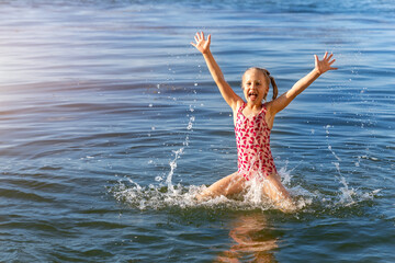 Fototapeta premium Cute adorable playful caucasian blond kid girl enjoy having fun swimming and splashing in clear blue water of sea or lake on hot summer day durin vacation holiday. Children outdoor healthy acivities