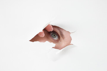Female eye looks through hole in white paper © H_Ko