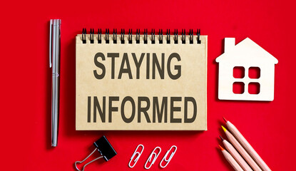 STAYING INFORMED text written on a notebook with pencils and office tools and model wooden house