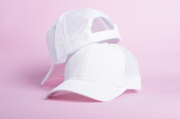 Two white baseball caps isolated on a pink background, front and back view, two blank trucker hats...