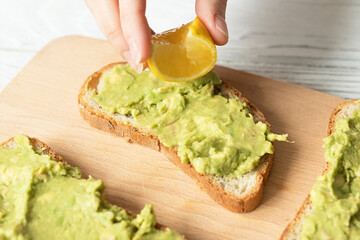 Pouring lemon juice on toast with guacamole, healthy vegan food