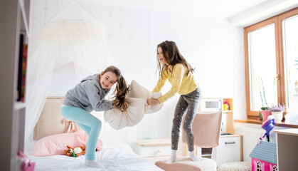 Two small girls sisters indoors at home, pillow fight in bedroom.